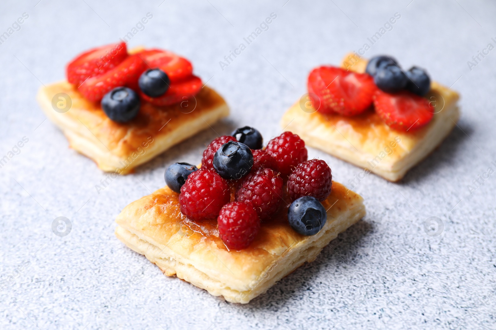 Photo of Tasty puff pastries with berries on light grey table, closeup