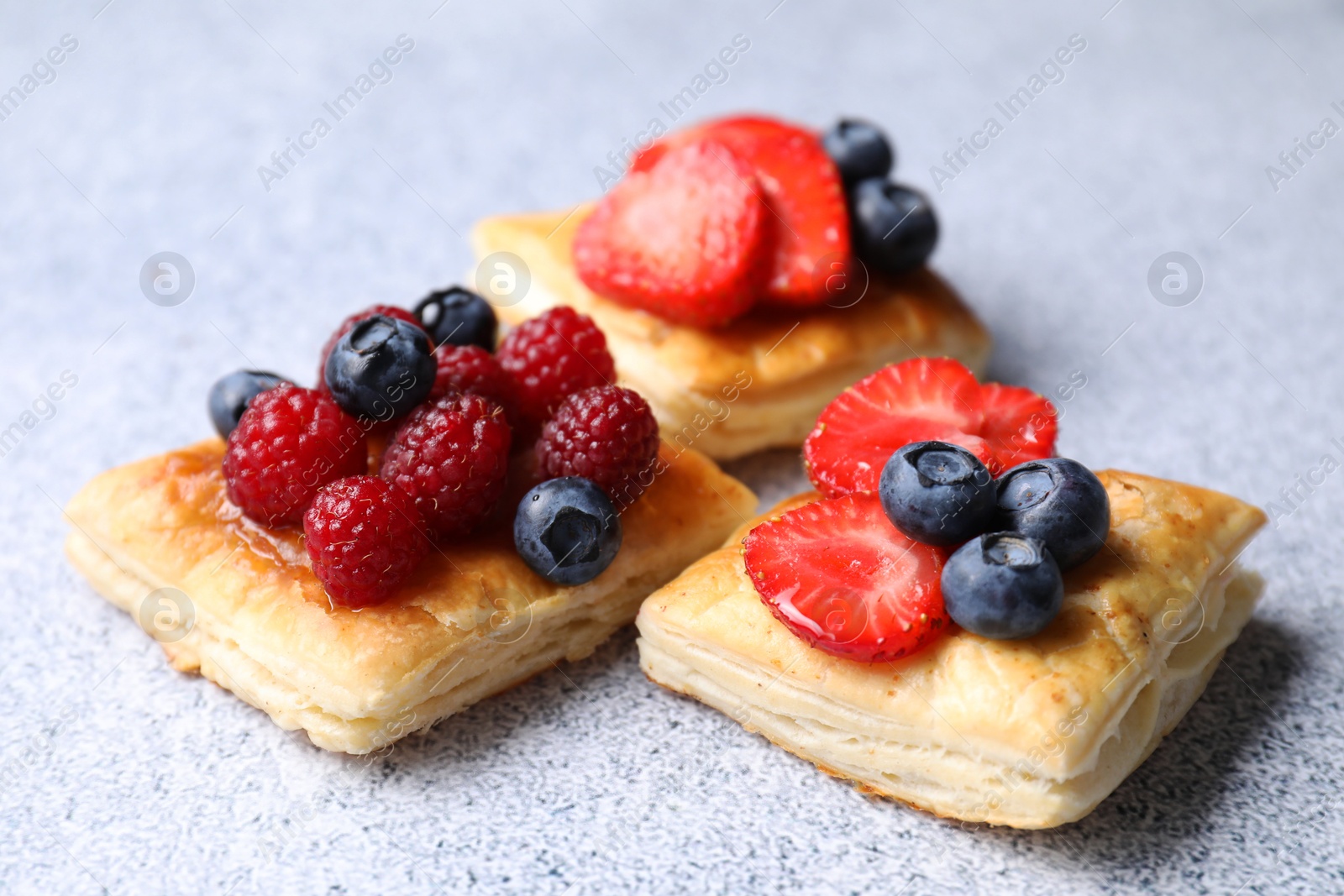 Photo of Tasty puff pastries with berries on light grey table, closeup