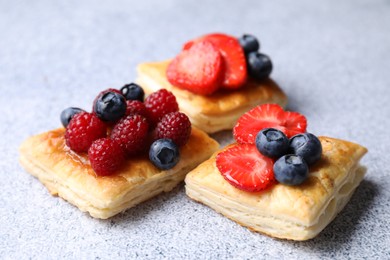 Tasty puff pastries with berries on light grey table, closeup