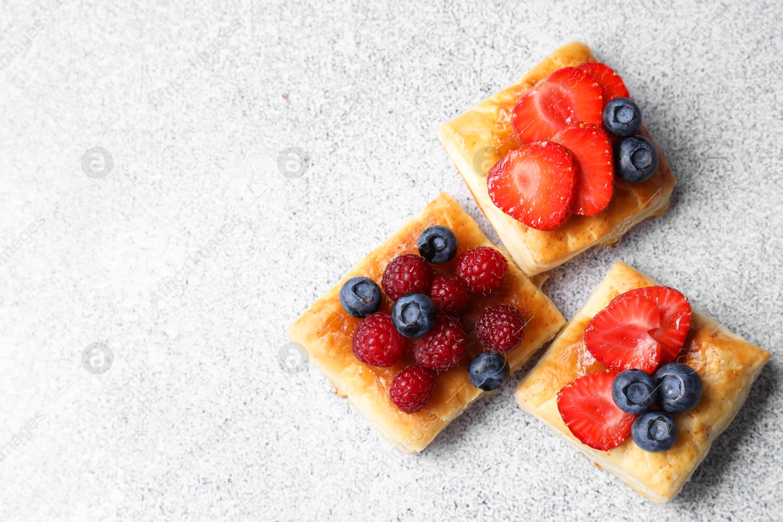 Photo of Tasty puff pastries with berries on light grey table, flat lay. Space for text