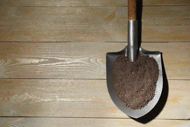 Photo of Metal shovel with soil on wooden table, top view. Space for text