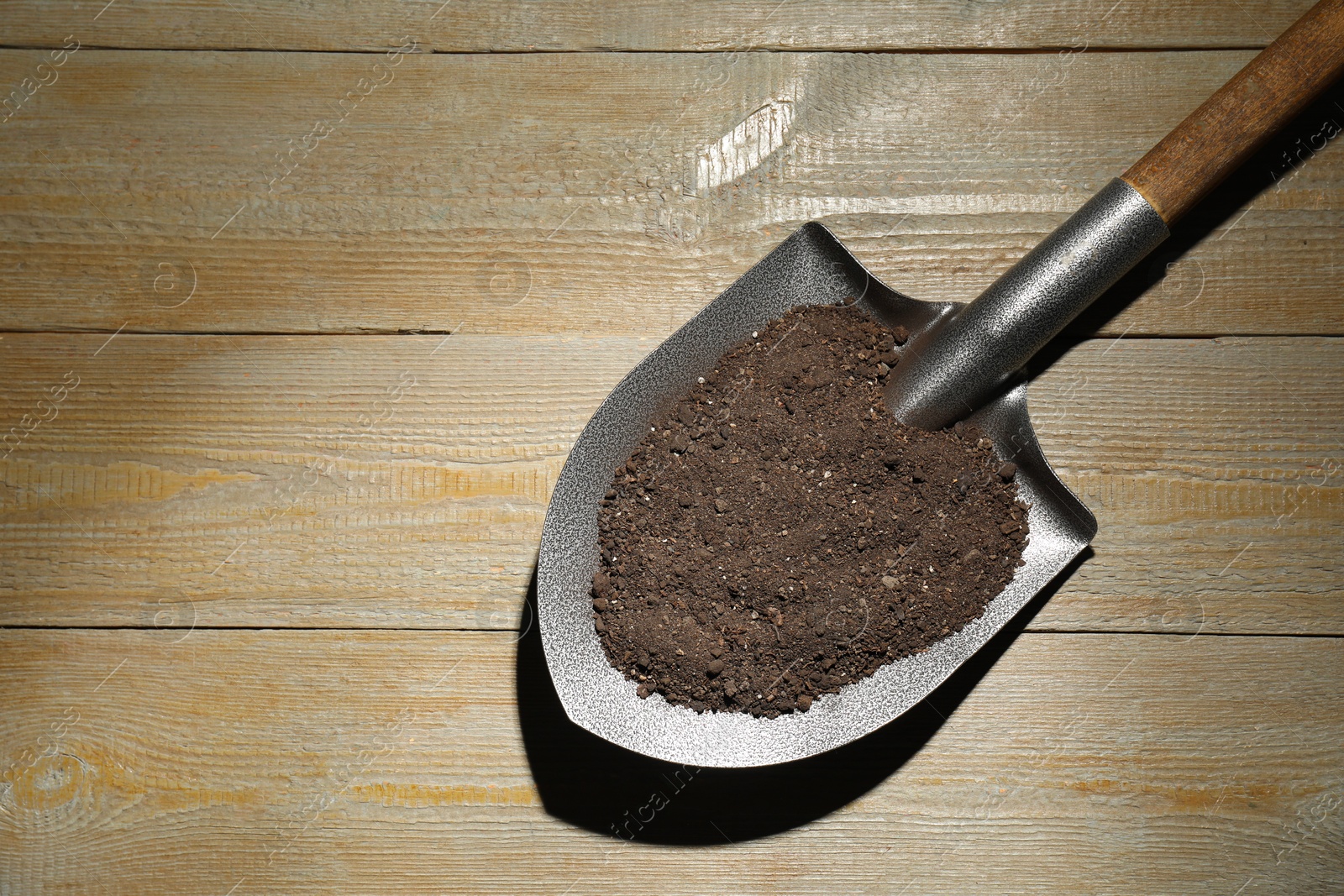 Photo of Metal shovel with soil on wooden table, top view. Space for text