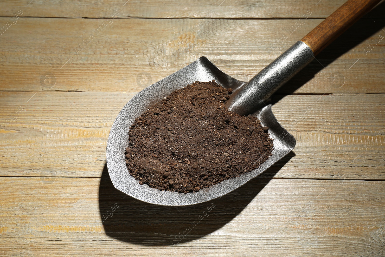 Photo of Metal shovel with soil on wooden table