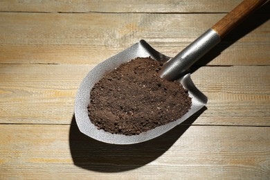 Photo of Metal shovel with soil on wooden table