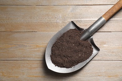 Photo of Metal shovel with soil on wooden table, top view. Space for text