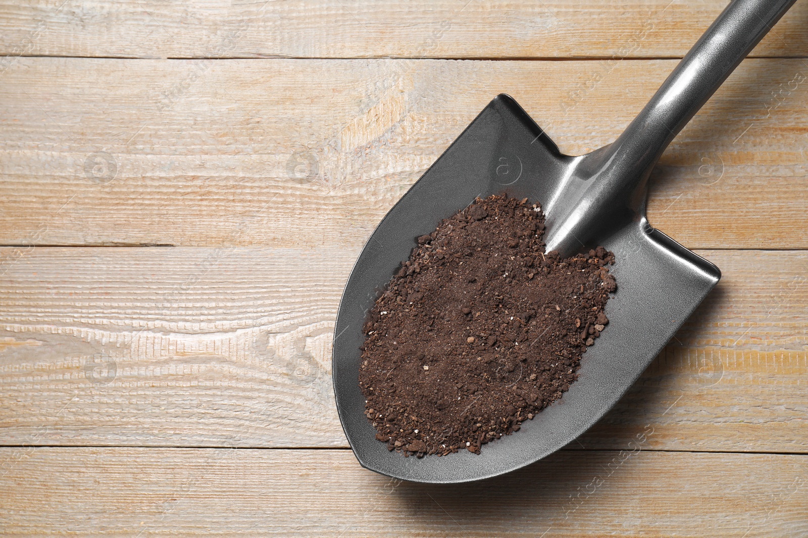 Photo of Metal shovel with soil on wooden table, top view. Space for text