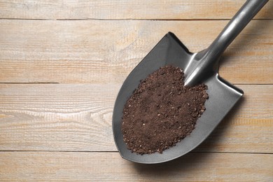 Photo of Metal shovel with soil on wooden table, top view. Space for text