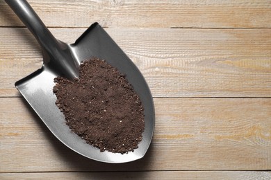 Photo of Metal shovel with soil on wooden table, top view. Space for text