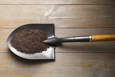 Photo of Metal shovel with soil on wooden table, top view