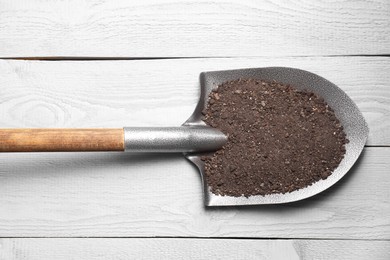 Photo of Metal shovel with soil on light grey wooden table, top view