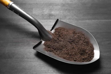 Photo of Metal shovel with soil on black wooden table