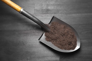 Photo of Metal shovel with soil on black wooden table, top view