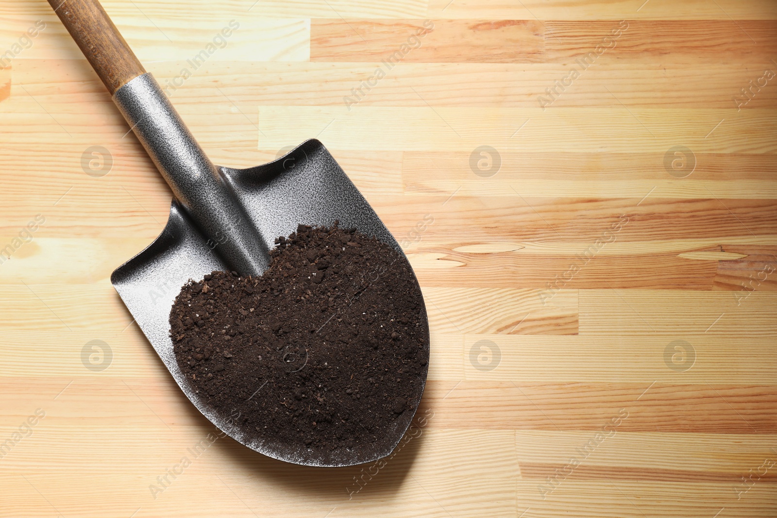 Photo of Metal shovel with soil on light wooden table, top view. Space for text