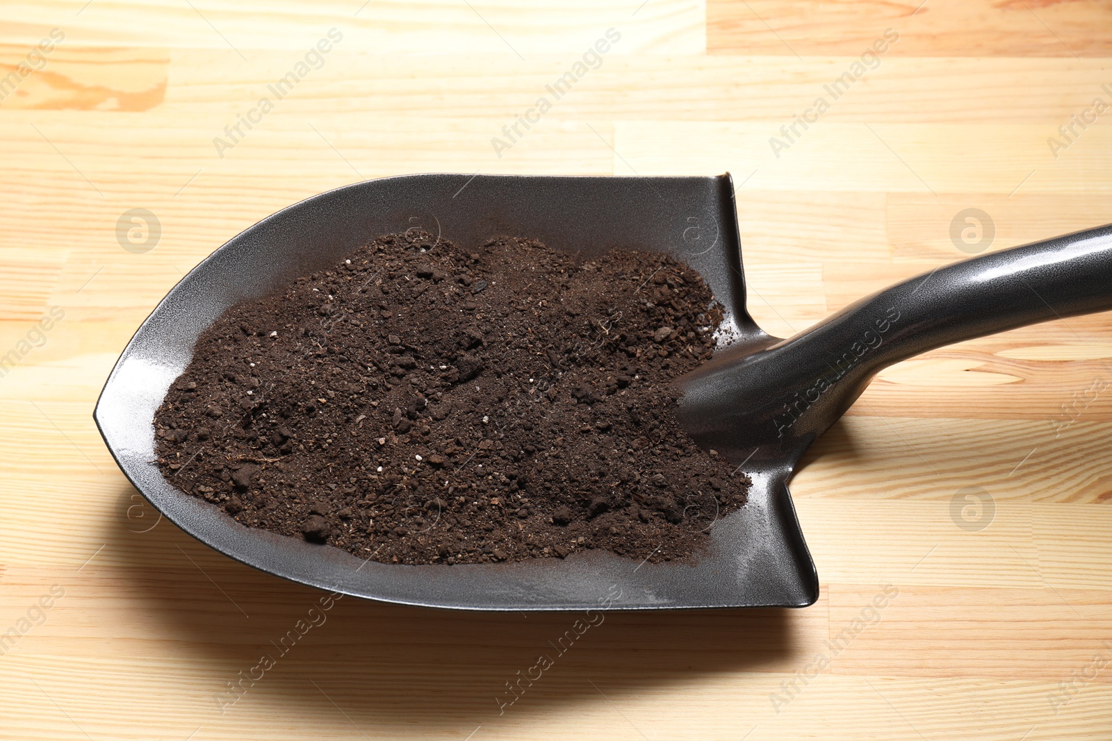 Photo of Metal shovel with soil on light wooden table, closeup