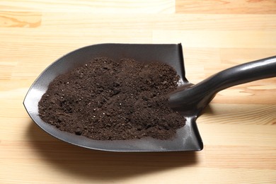 Photo of Metal shovel with soil on light wooden table, closeup