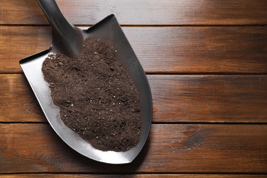 Photo of Metal shovel with soil on wooden table, top view. Space for text