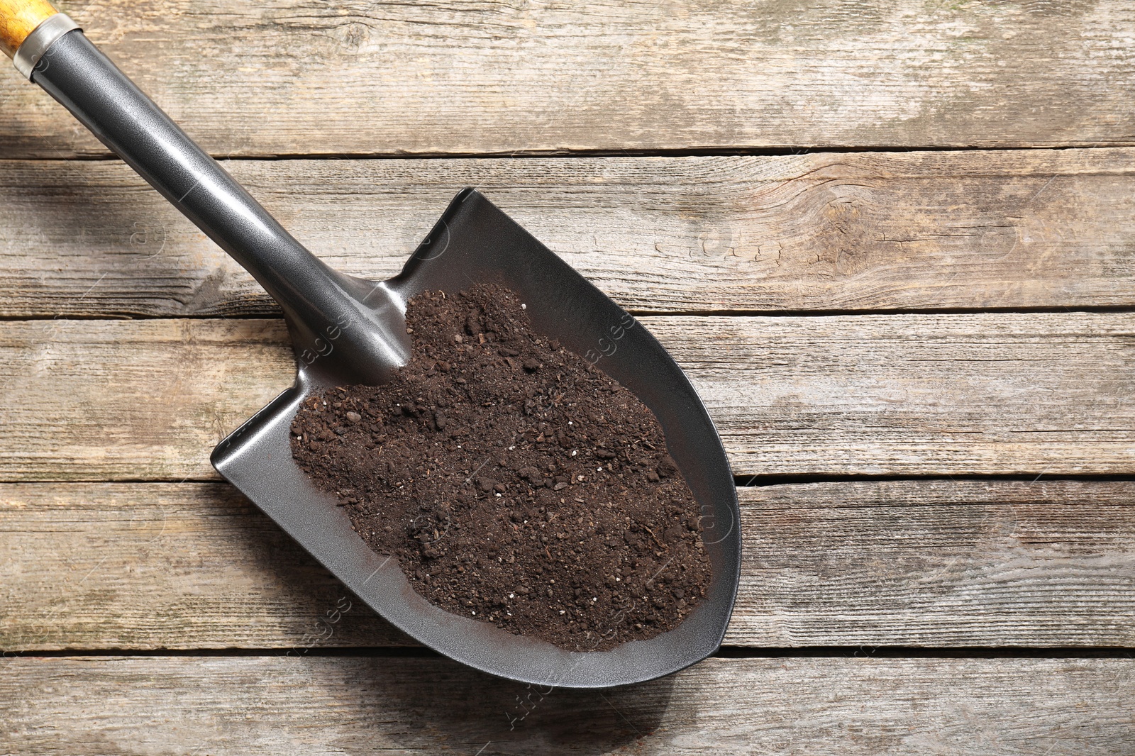 Photo of Metal shovel with soil on wooden table, top view. Space for text