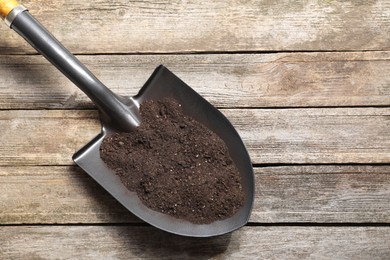 Photo of Metal shovel with soil on wooden table, top view. Space for text