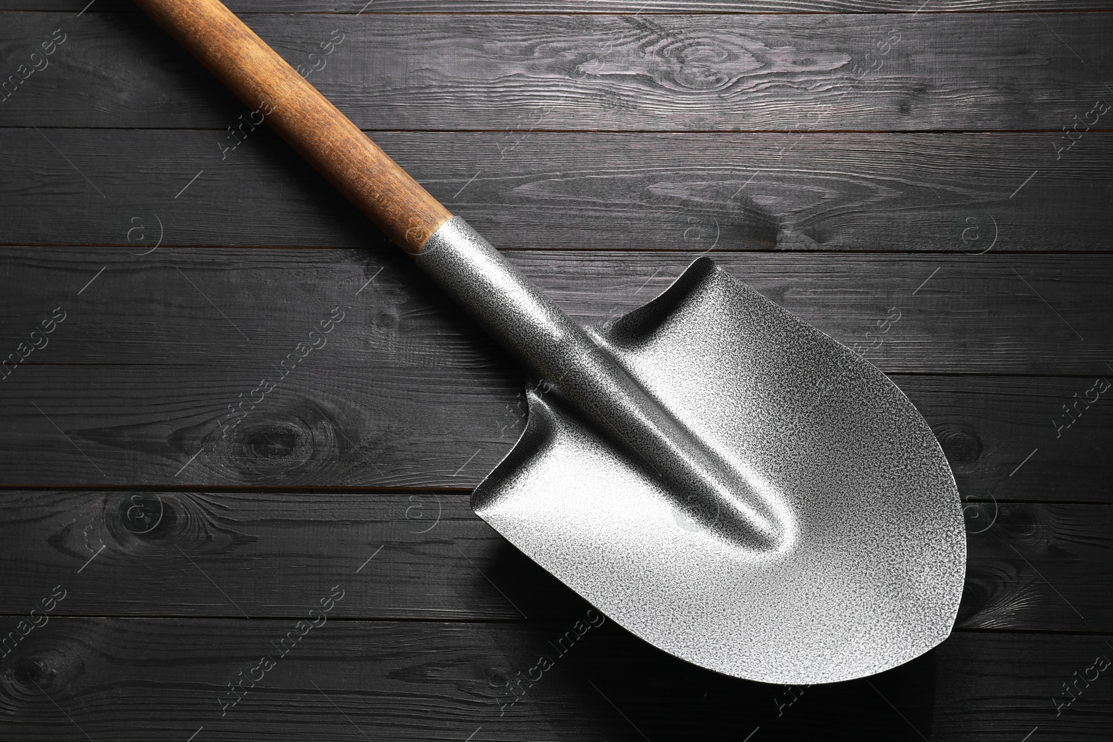 Photo of Metal shovel on black wooden table, top view