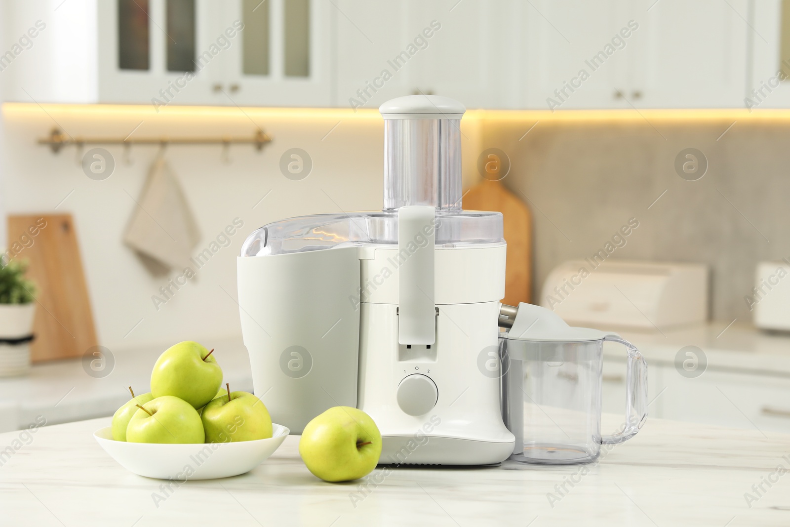 Photo of Modern juicer and apples on white marble table in kitchen