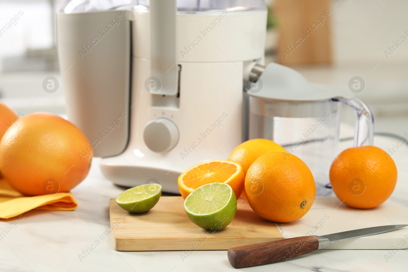 Photo of Modern juicer, oranges and limes on white marble table in kitchen, closeup