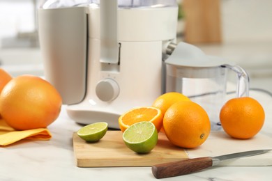 Modern juicer, oranges and limes on white marble table in kitchen, closeup