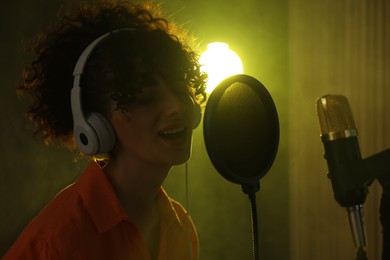 Photo of Vocalist wearing headphones singing into microphone in professional record studio with smoke and lights