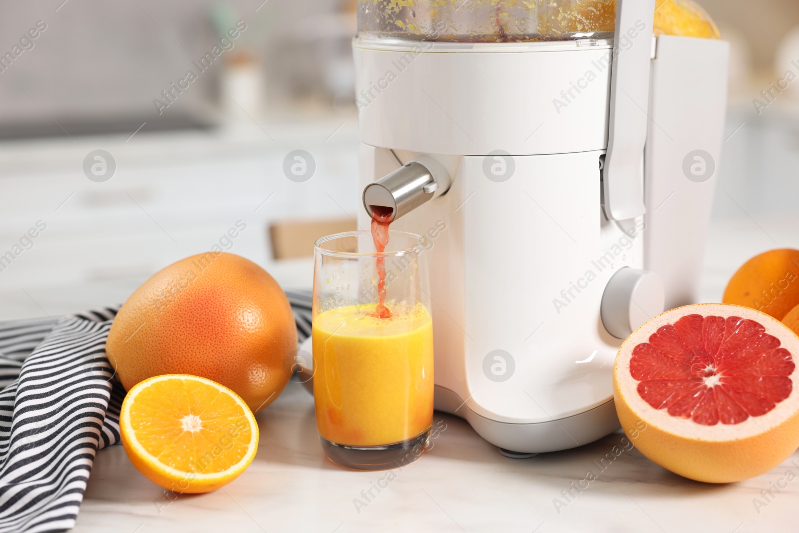 Photo of Modern juicer, oranges, grapefruits and glass on white marble table in kitchen