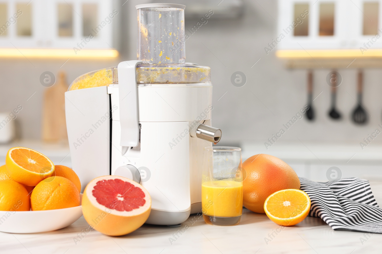 Photo of Modern juicer, oranges, grapefruits and glass on white marble table in kitchen