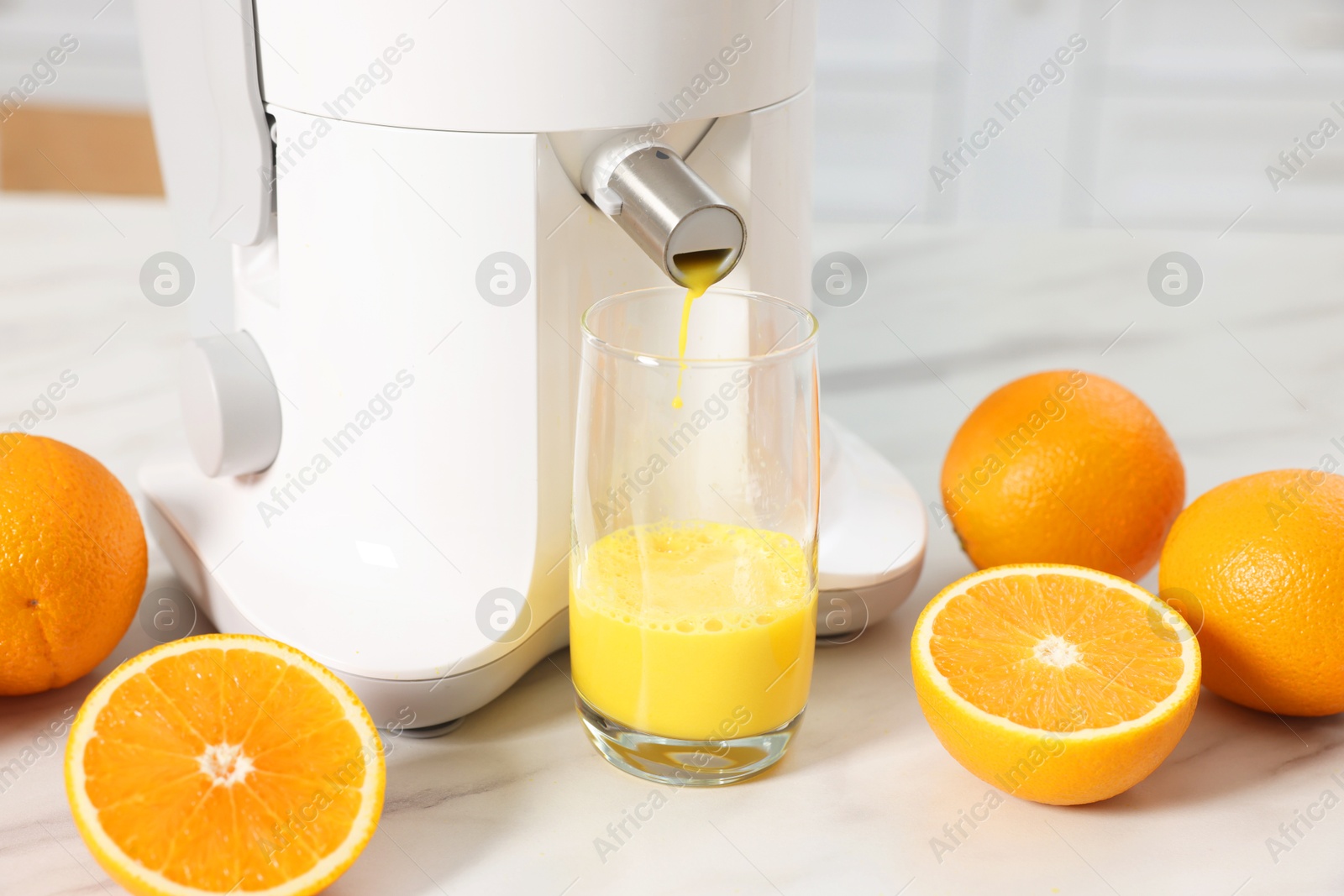 Photo of Modern juicer, oranges and glass on white marble table in kitchen, closeup