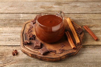 Tasty melted chocolate in cup and spices on wooden table, closeup