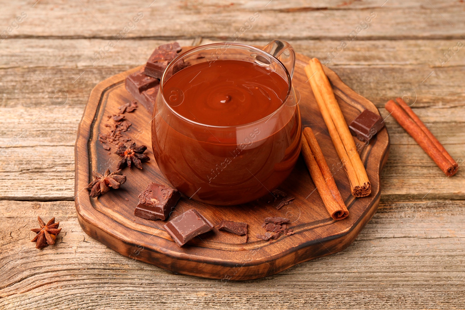 Photo of Tasty melted chocolate in cup and spices on wooden table, closeup