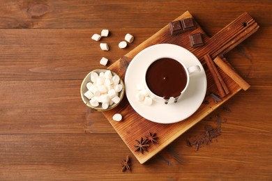 Photo of Tasty melted chocolate in cup, marshmallows and spices on wooden table, flat lay. Space for text