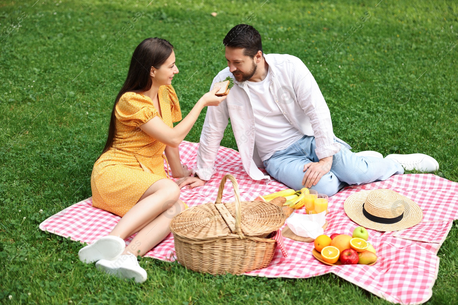 Photo of Romantic picnic. Woman feeding her boyfriend on blanket outdoors