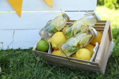 Photo of Refreshing lemonade with mint and fresh fruits in wooden crate on green grass outdoors