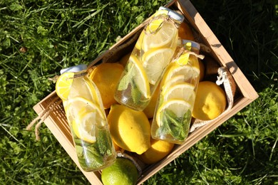 Photo of Refreshing lemonade with mint and fresh fruits in wooden crate on green grass outdoors, top view