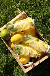 Photo of Refreshing lemonade with mint and fresh fruits in wooden crate on green grass outdoors, top view