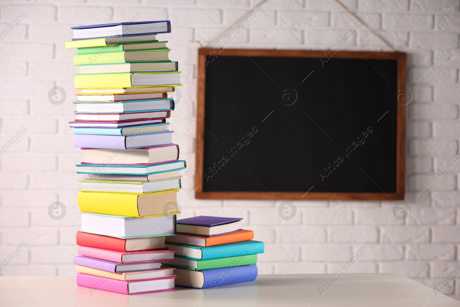 Photo of Stacks of many colorful books on white wooden table in classroom. Space for text