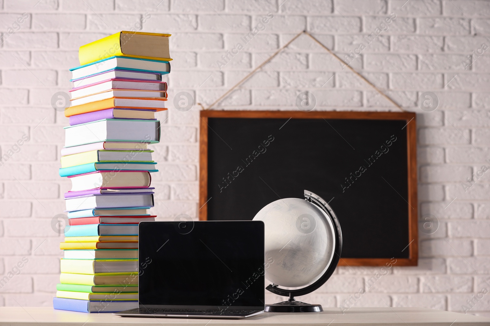 Photo of Stack of many colorful books, laptop and globe on white wooden table in classroom. Space for text