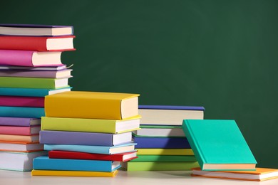 Stacks of many colorful books on white table near chalkboard in classroom. Space for text