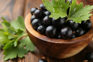 Ripe black currants and leaves in bowl on wooden table, closeup