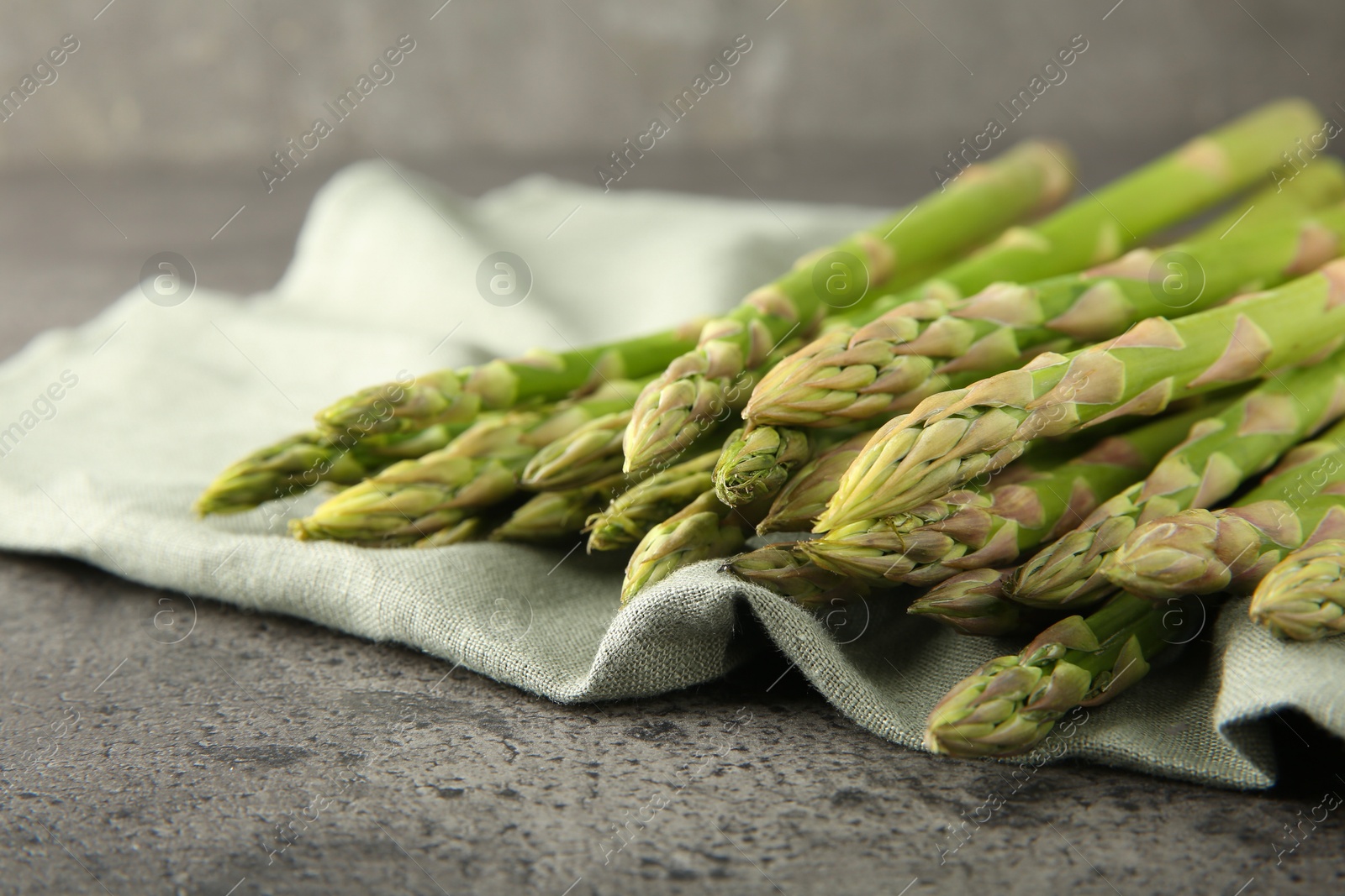 Photo of Fresh green asparagus stems on grey textured table, closeup