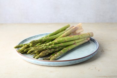 Photo of Plate with fresh green asparagus stems on light textured table, closeup