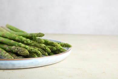 Photo of Plate with fresh green asparagus stems on light textured table, closeup. Space for text