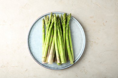 Photo of Plate with fresh green asparagus stems on light textured table, top view