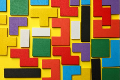 Colorful wooden puzzle pieces on yellow background, top view