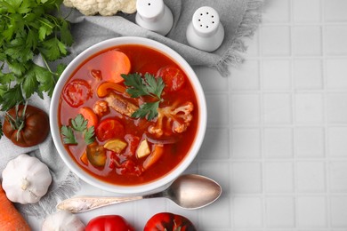 Photo of Delicious homemade stew in bowl, spoon and ingredients on white tiled table, flat lay. Space for text