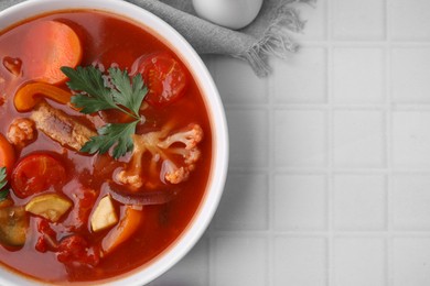 Delicious homemade stew in bowl on white tiled table, top view. Space for text