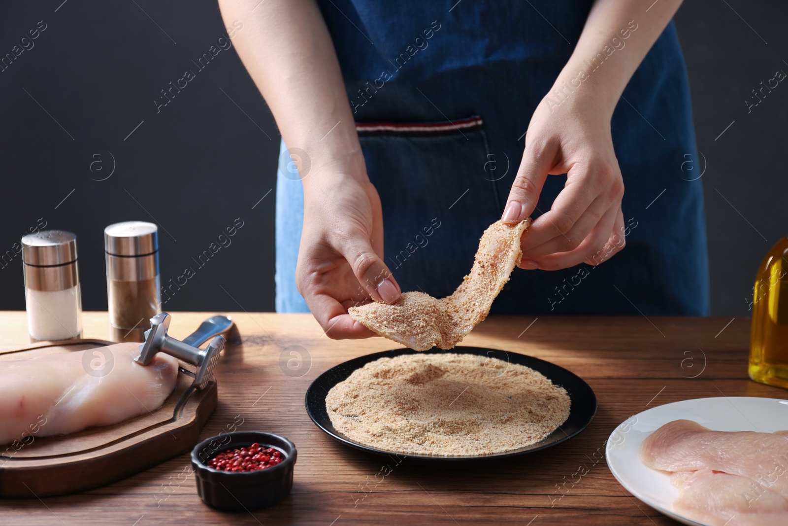 Photo of Making schnitzel. Woman coating slice of meat with bread crumbs at wooden table, closeup