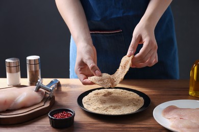 Photo of Making schnitzel. Woman coating slice of meat with bread crumbs at wooden table, closeup